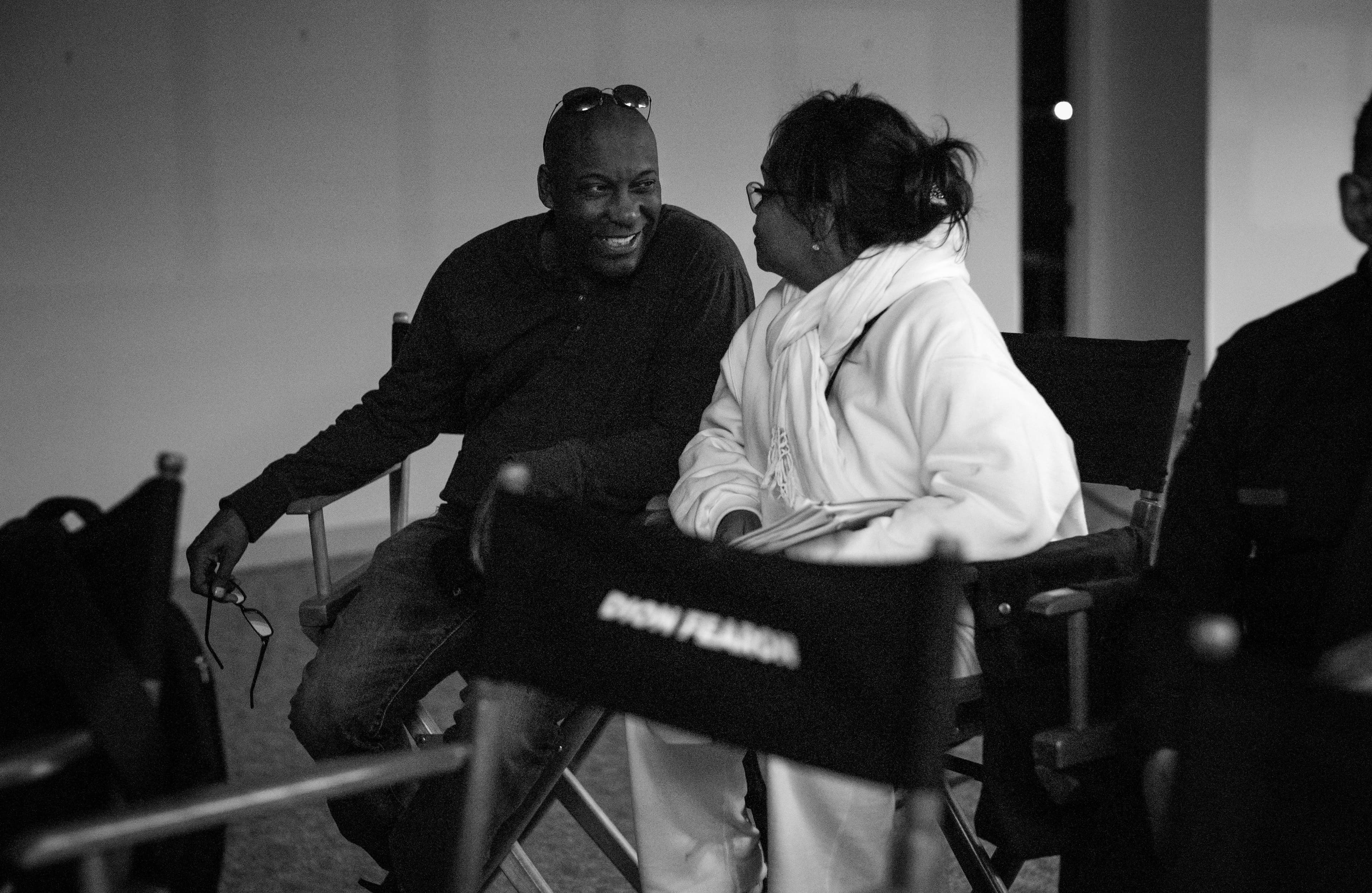 John Singleton and founder Dion Fearon talking in director's chairs on set, her name printed on the chair back